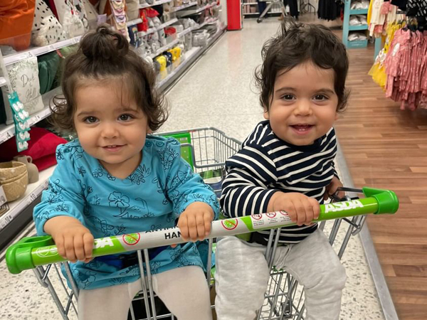 Two twins sit in a supermarket twin trolley