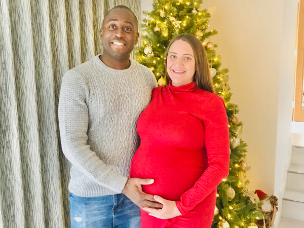 A couple stand together, the woman is pregnant and the man stands with his hand on her bump