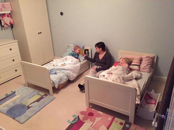 A mother sits in between two small beds with children in them