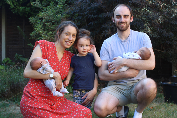 A family including a daughter and two twins sit on the grass smiling at the camera