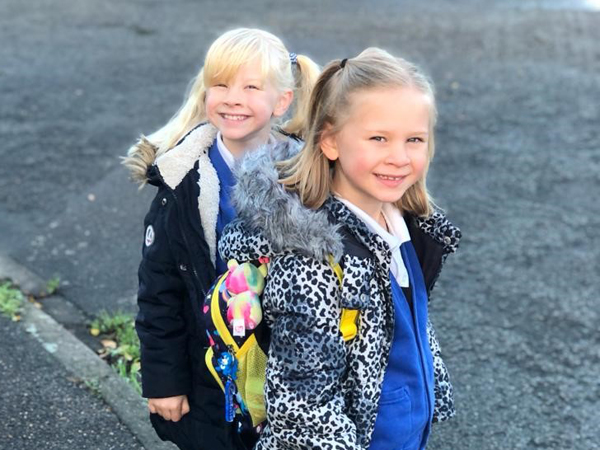 Two girls in school uniform smile, looking sideways at the camera