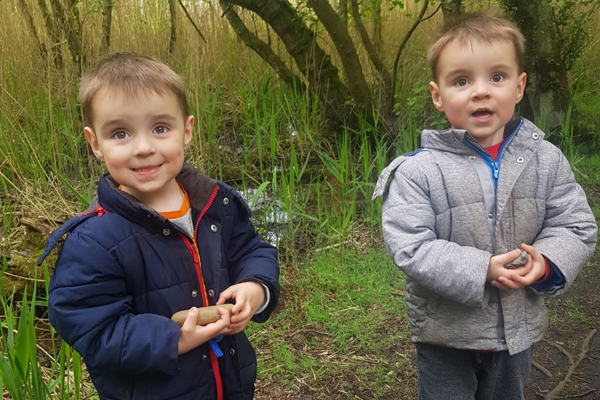 Two children stood in a wooded area looking at the camera