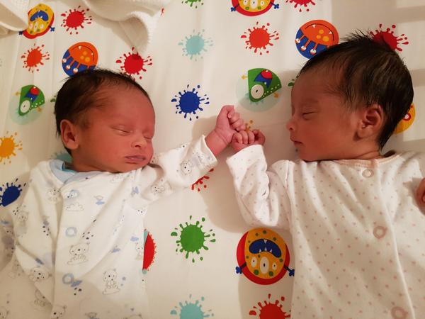 Two newborn twins lie sleeping next to each other with their hands touching